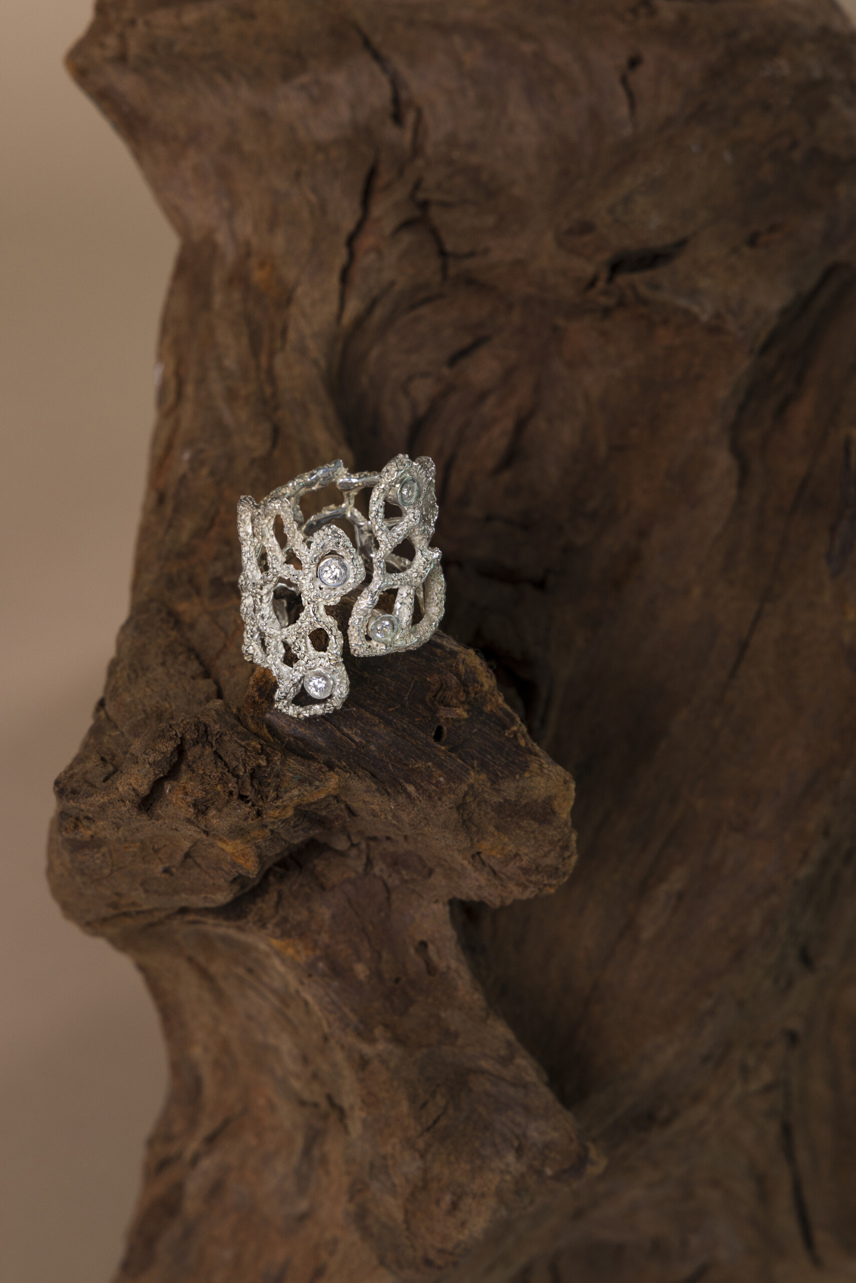 Anello a fascia larga Nebula in argento, caratterizzato da un design aperto regolabile e una lavorazione a cera persa, poggiato su legno scuro.