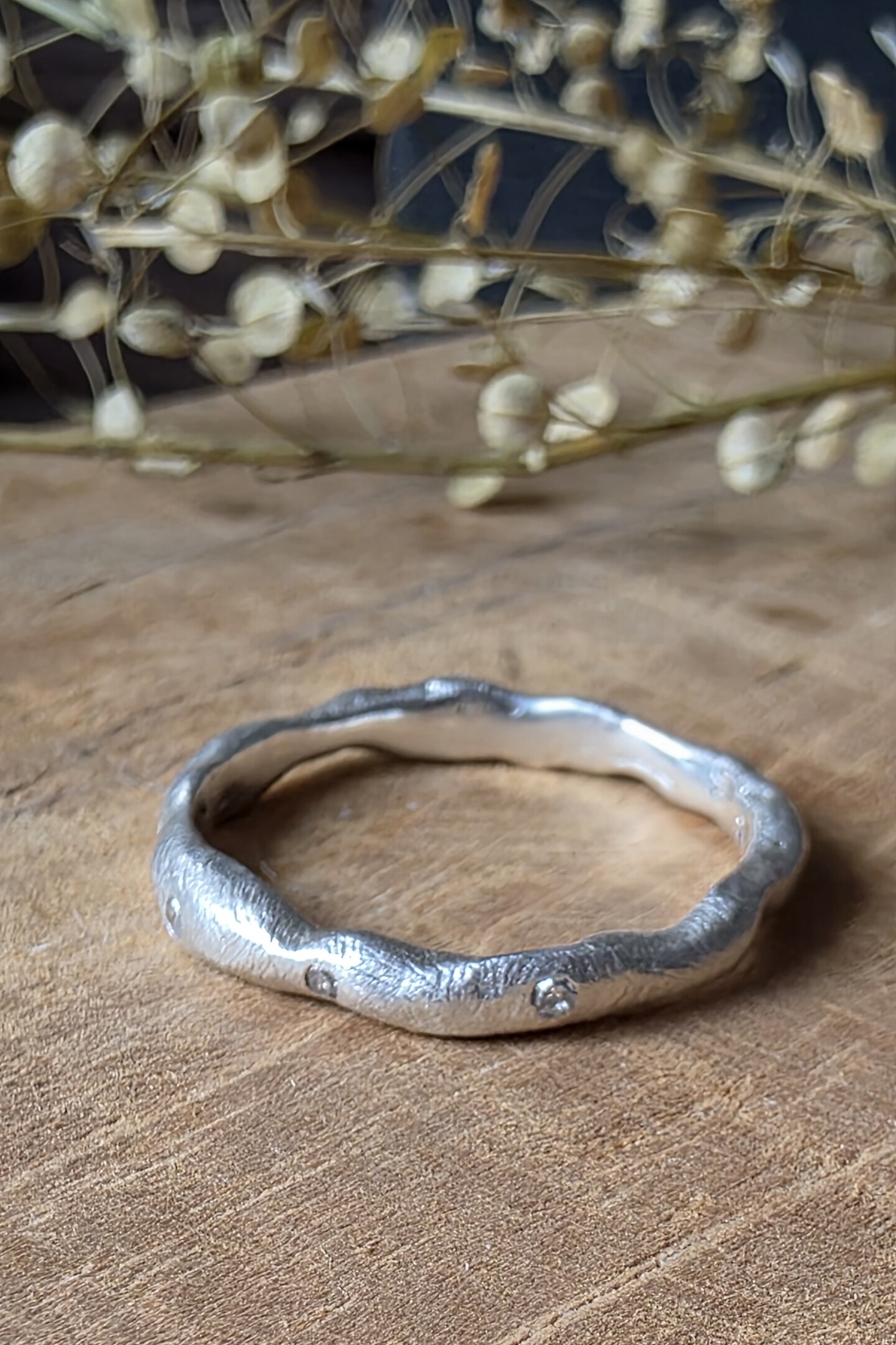 Anello artigianale Caleidos in argento satinato con dieci diamanti naturali incastonati, esposto su legno