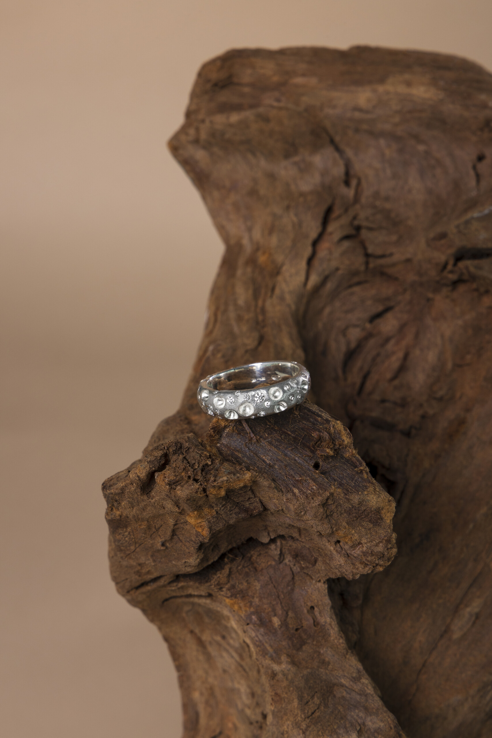 Anello artigianale realizzato a cera persa con zirconi, poggiato su una base di legno scuro nel nostro laboratorio orafo.