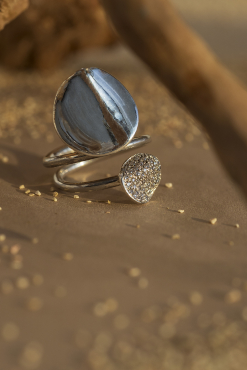 Anello artigianale della collezione Moon con design a tre fili, mostrante una luna in argento lucido e una con pavé di zirconi su fondo sabbioso.