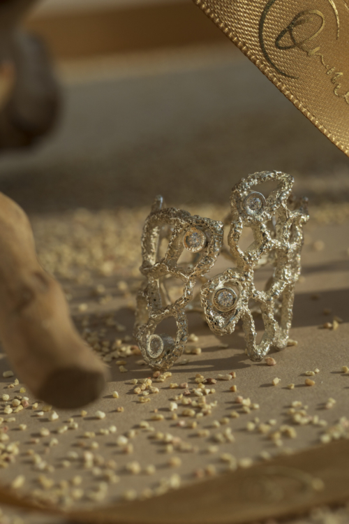 Primo piano macro dell'anello Nebula in argento con zirconi incastonati; la struttura organica e materica è affiancata da un nastro dorato del brand.