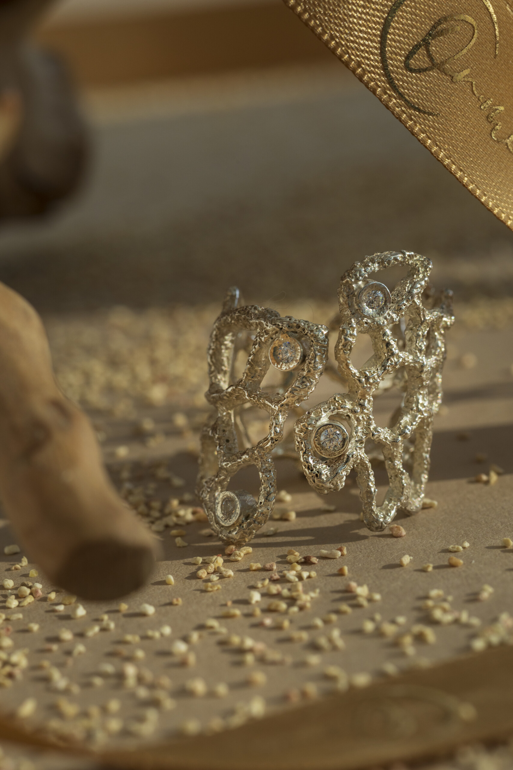 Primo piano macro dell'anello Nebula in argento con zirconi incastonati; la struttura organica e materica è affiancata da un nastro dorato del brand.