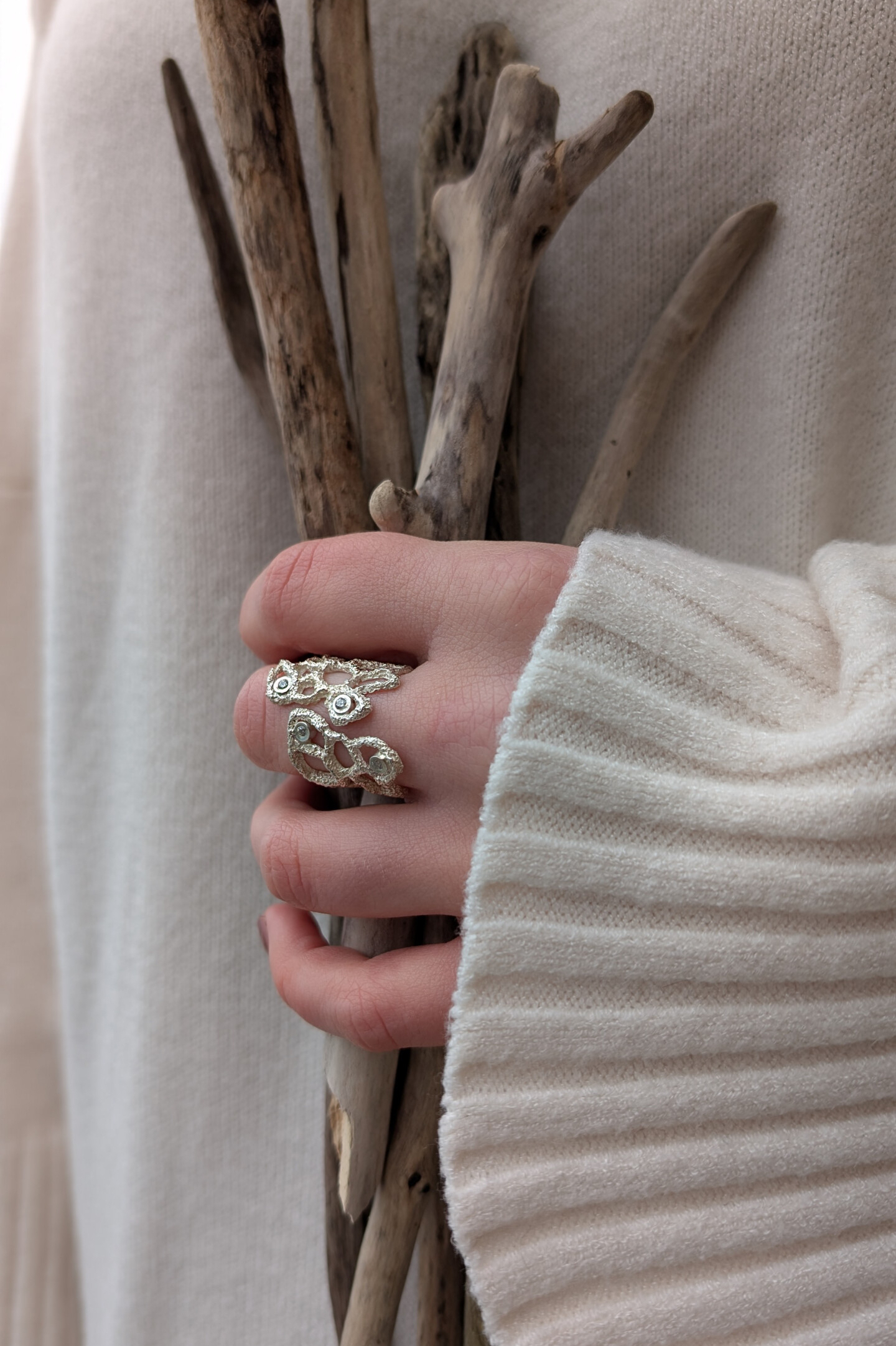 Mano che indossa l'anello a fascia Nebula mentre stringe dei rami secchi, mostrando come il gioiello si adatti perfettamente alla forma delle dita.