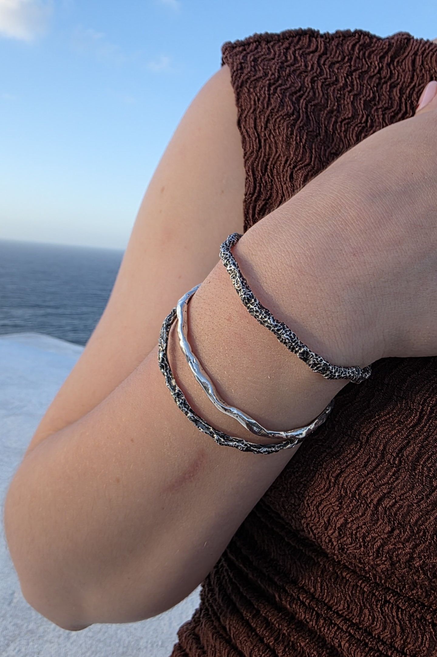 Tre bracciali della collezione Tephra indossati: al centro il modello Lava in argento lucido risalta tra i modelli bruniti. Gioielli artigianali Orme.