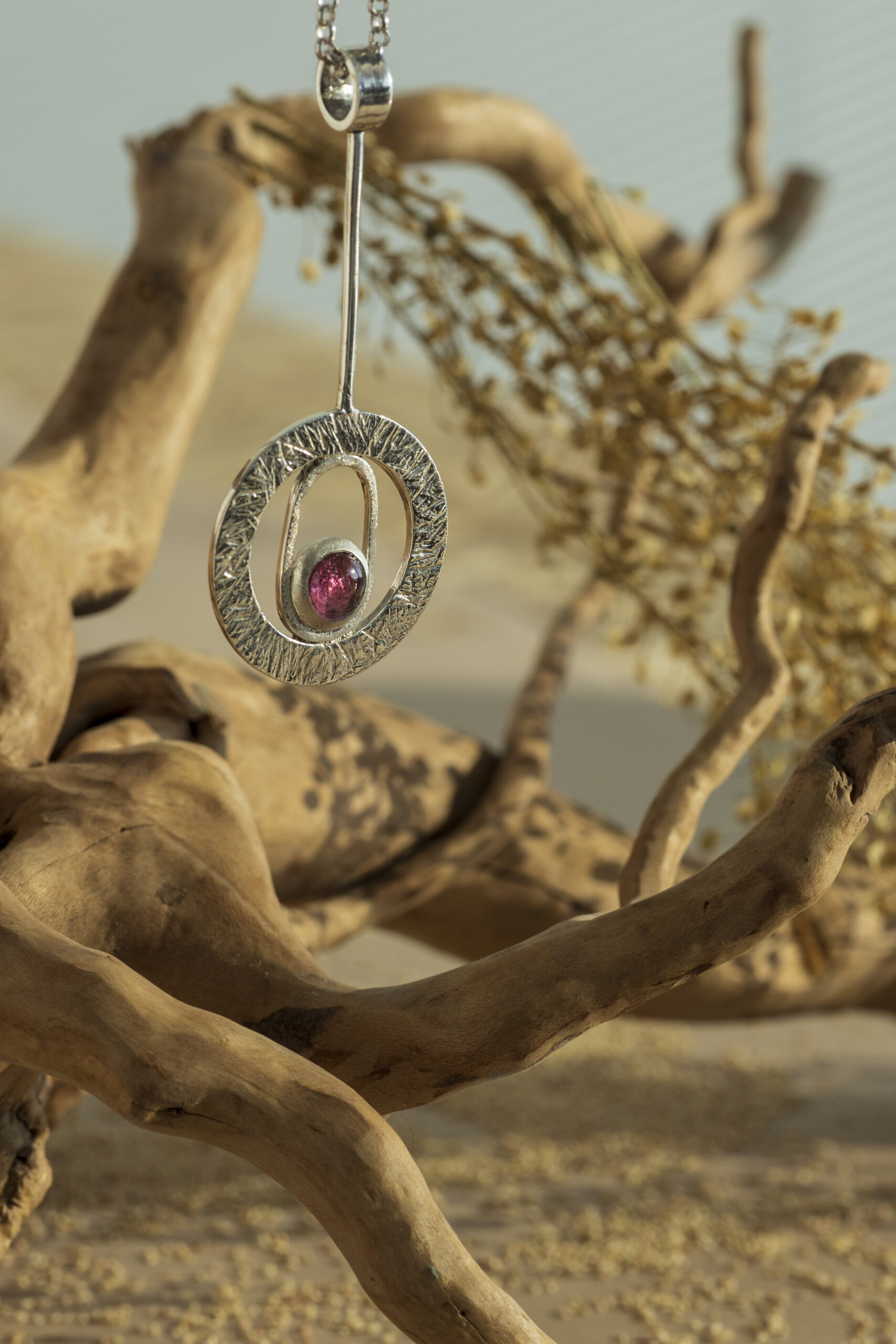 Pendente circolare stile anni 70 in argento con castone centrale e pietra tormalina rosa su sfondo naturale.