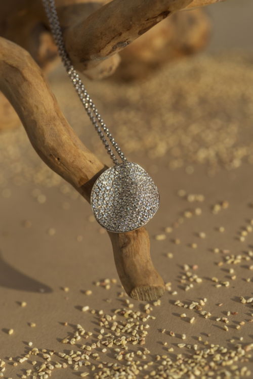 Girocollo artigianale della collezione Moon con pendente a forma di luna piena ricoperto da un pavé di zirconi luminosi, sospeso su un ramo naturale.