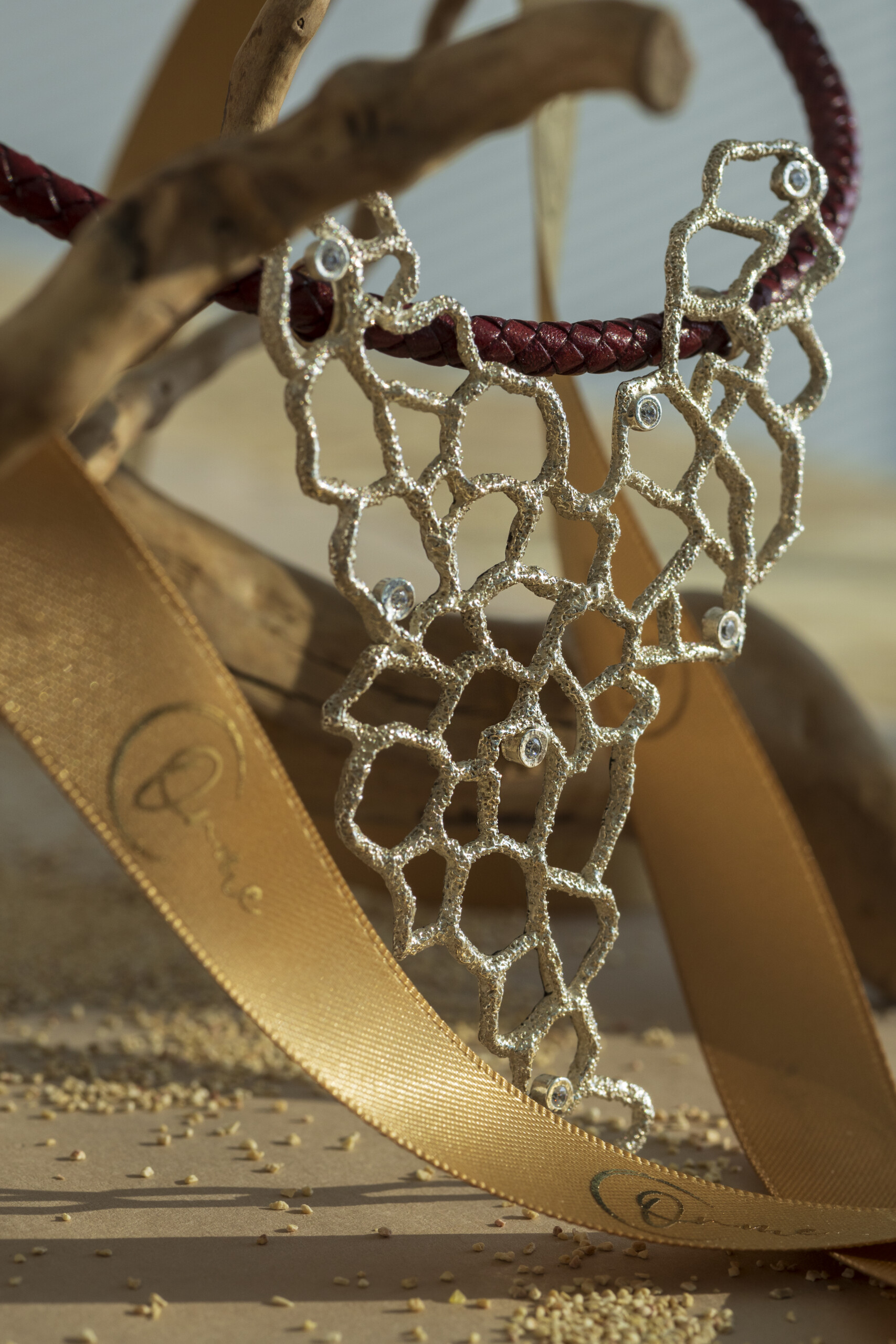 Collana con pendente a rete traforata della collezione Nebula in argento o oro con piccoli punti luce incastonati, con girocollo in pelle.