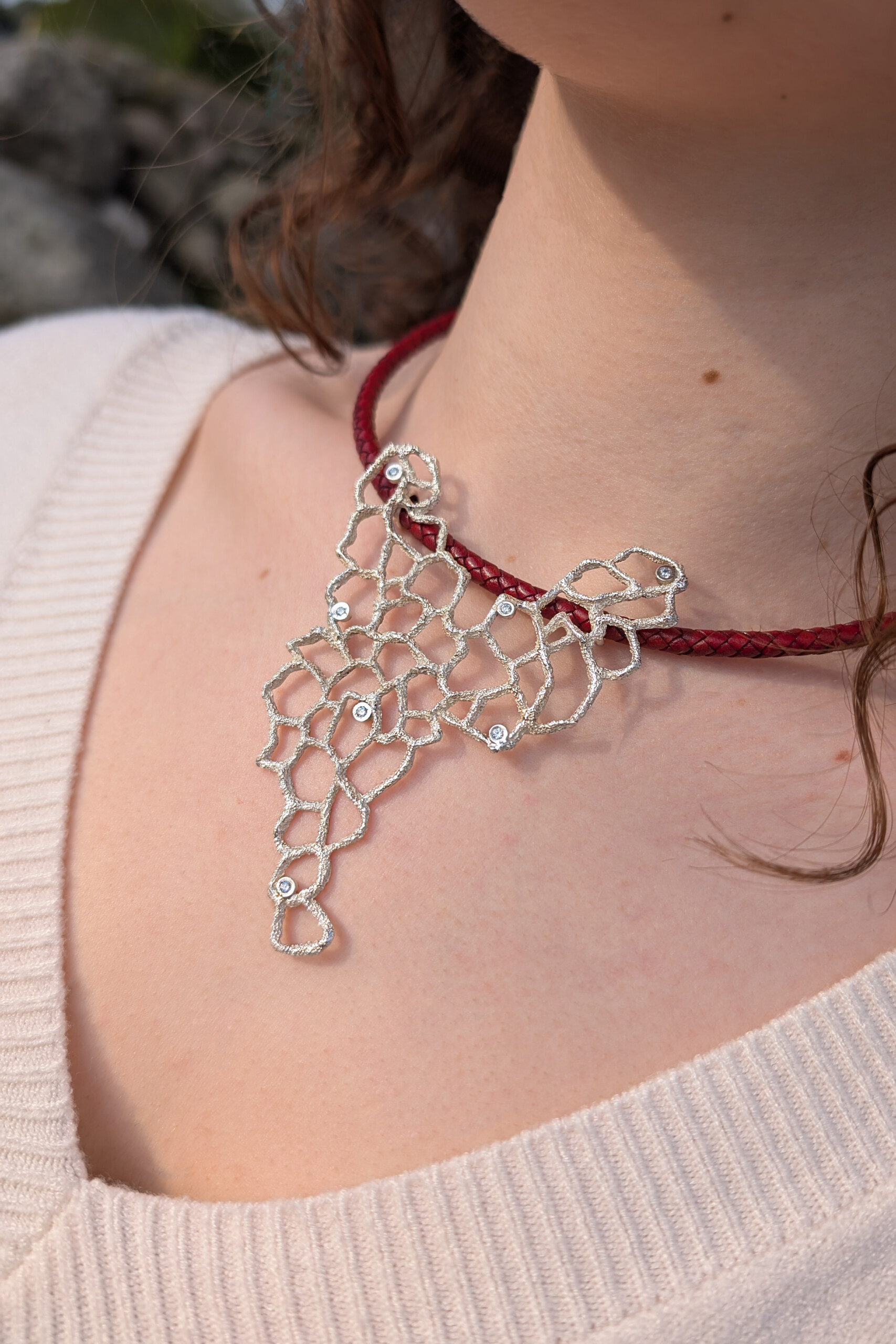 Foto lifestyle di una donna che indossa il girocollo Nebula; il pendente in argento e la pelle bordeaux risaltano sull'incarnato, realizzato nel nostro laboratorio ecommerce di gioielli.