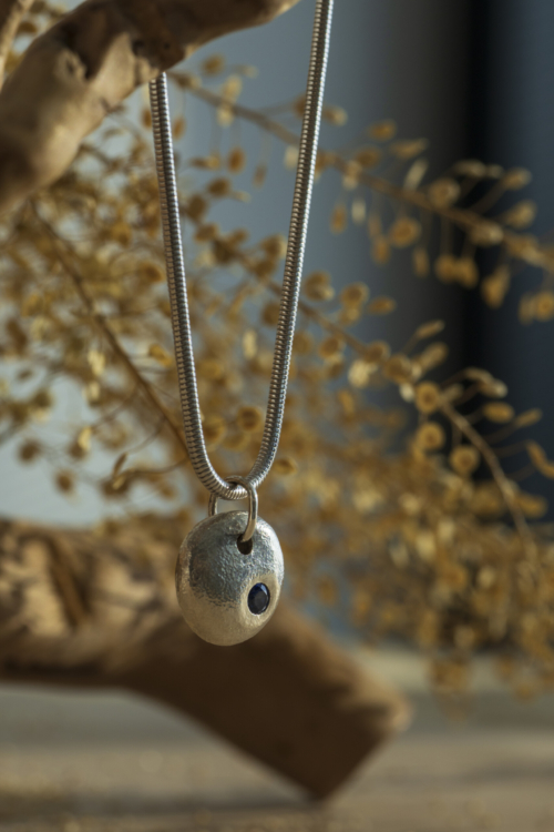 Ciondolo artigianale martellato della collezione Pepita con zaffiro blu incastonato, con catena coda di topo; un gioiello materico in argento 925.