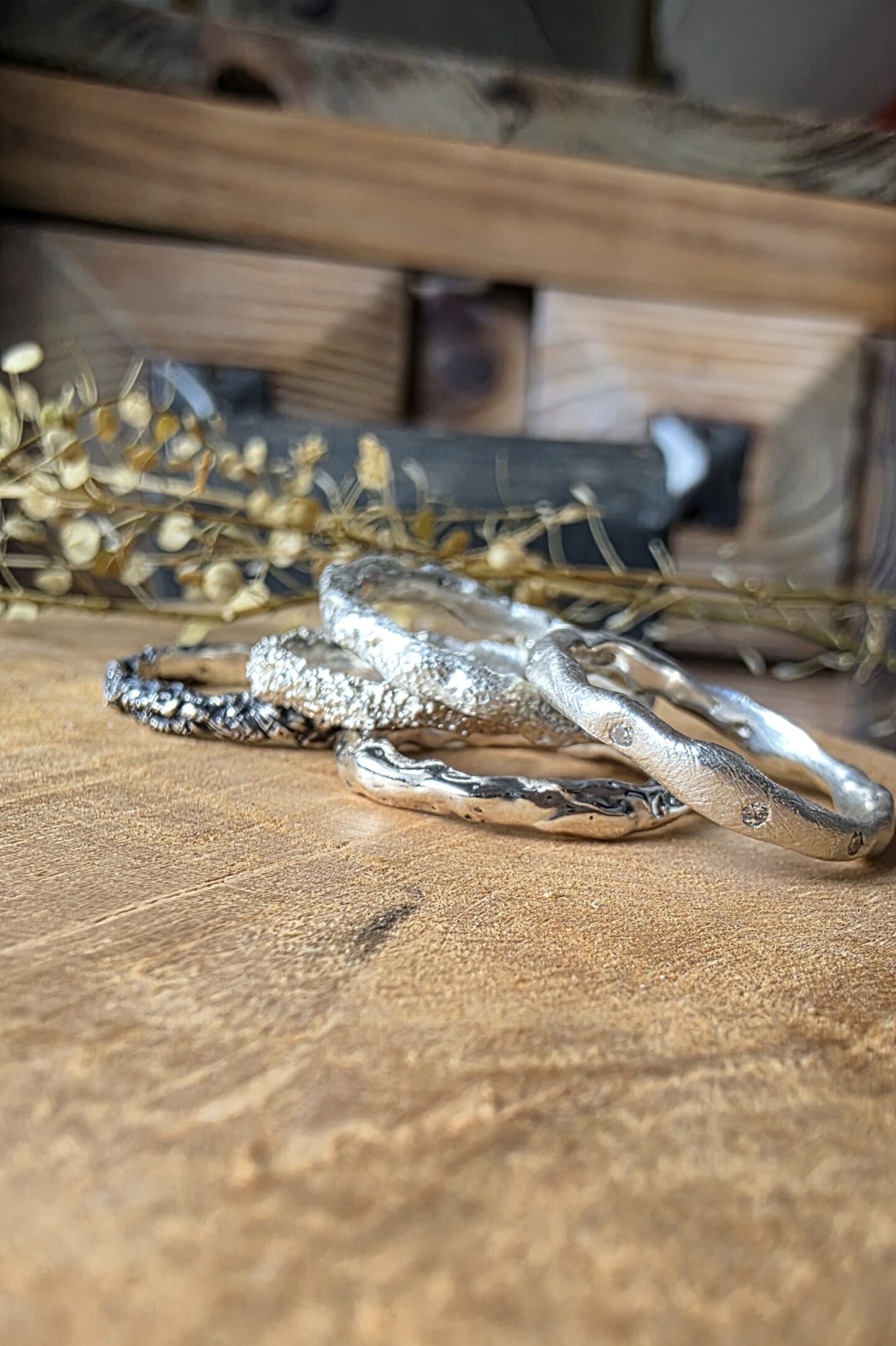 Insieme di cinque anelli artigianali Caleidos in argento 925 con diverse texture e diamanti naturali su base di legno.