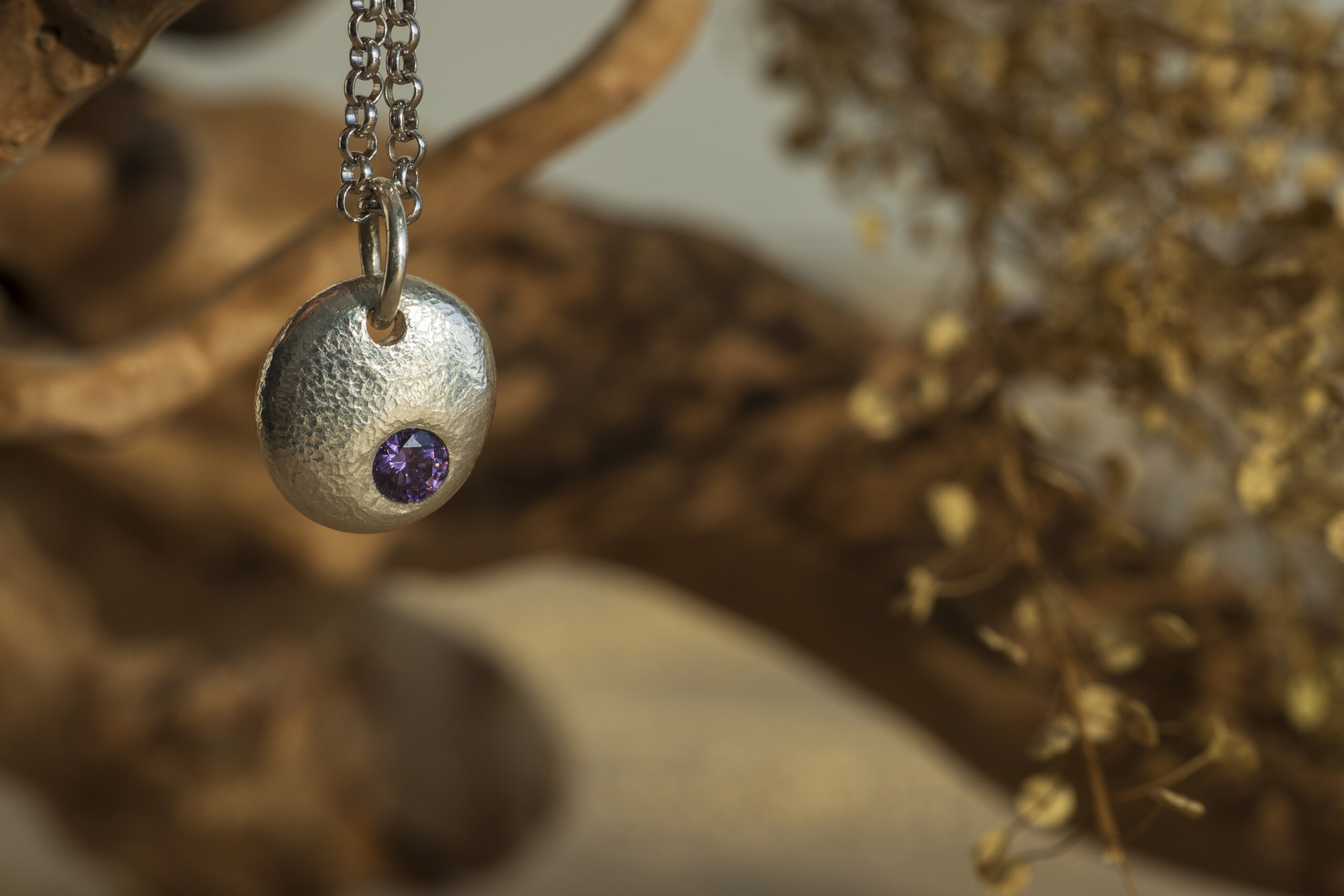 Ciondolo artigianale in argento satinato a forma di pepita con pietra naturale incastonata, sospeso su una catena sottile.