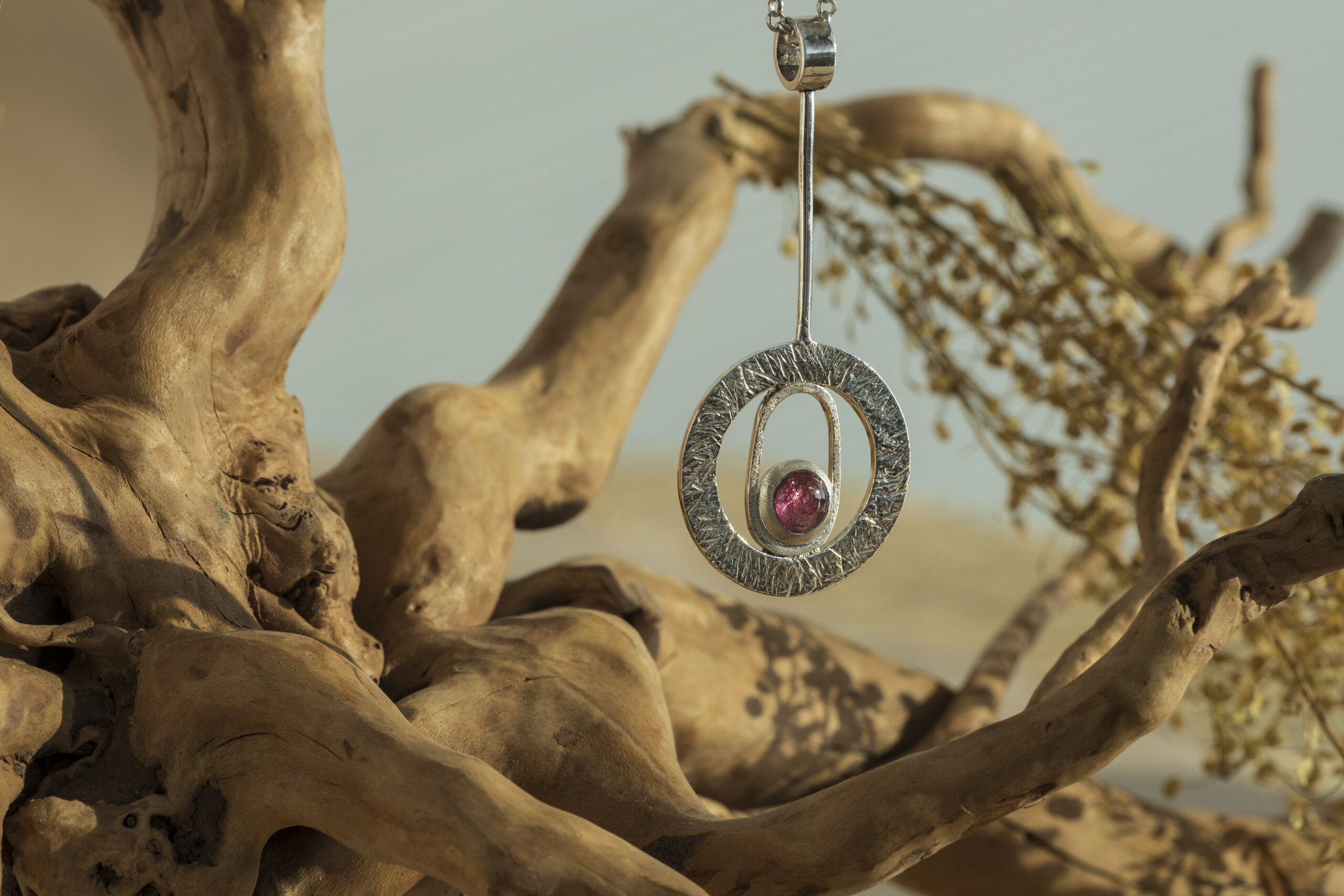 copertina-collezione-seventy-collana-argento-design-geometrico.jpg Pendente geometrico in argento materico stile anni 70 della collezione Seventy con tormalina naturale, esposto su rami naturali.