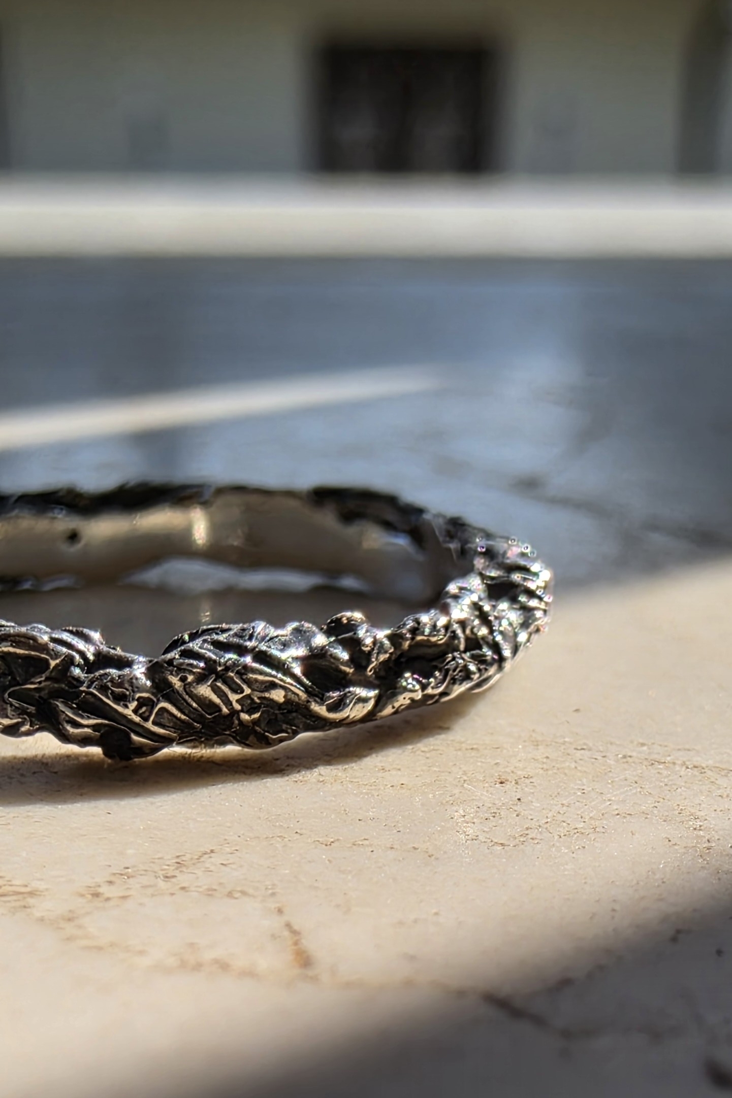 Macro superficie materica anello argento brunito con riflessi lucidi organici.