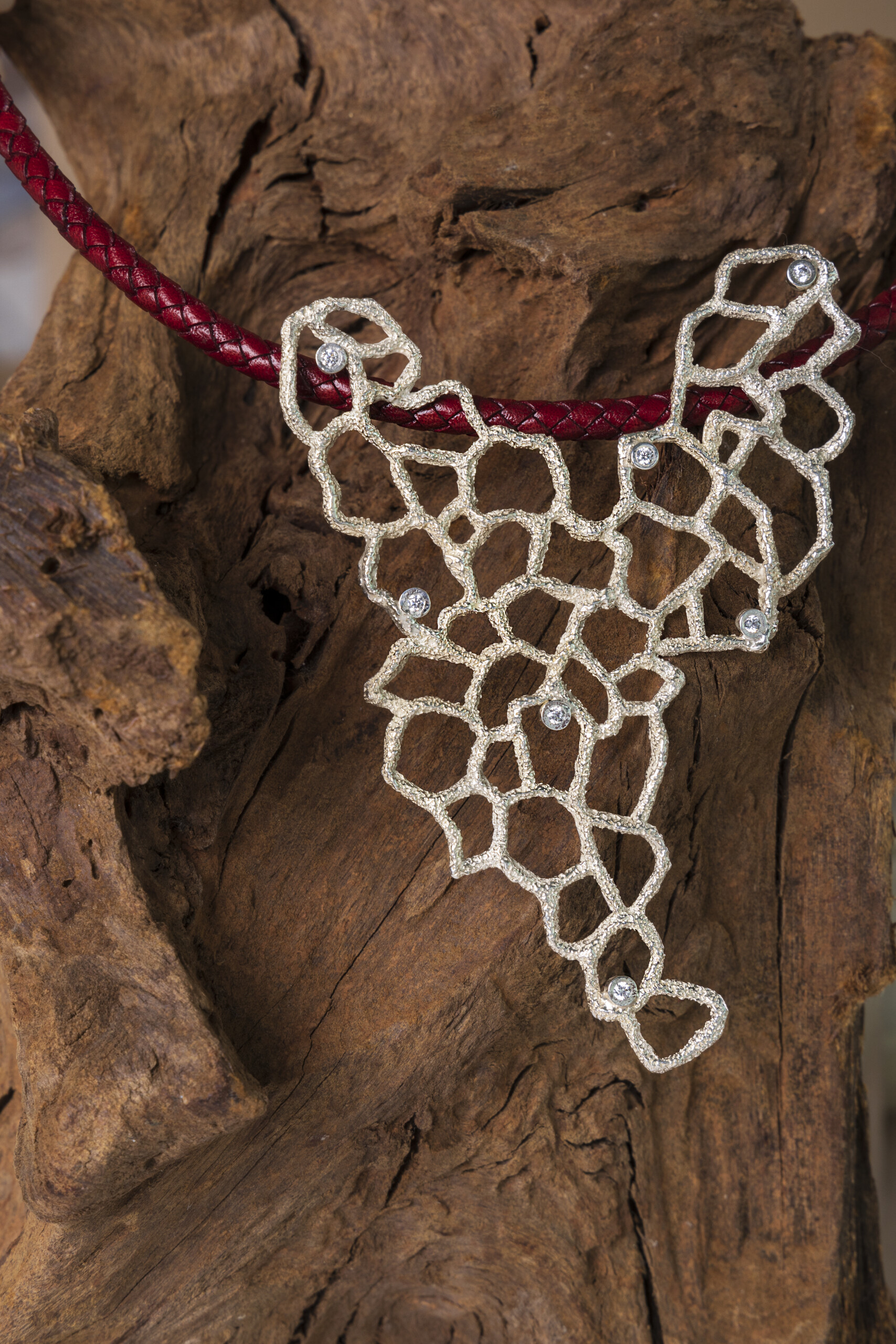 Il grande pendente Nebula in argento appoggiato su una radice di legno scuro; un gioiello artigianale modellato in cera persa nel nostro laboratorio.