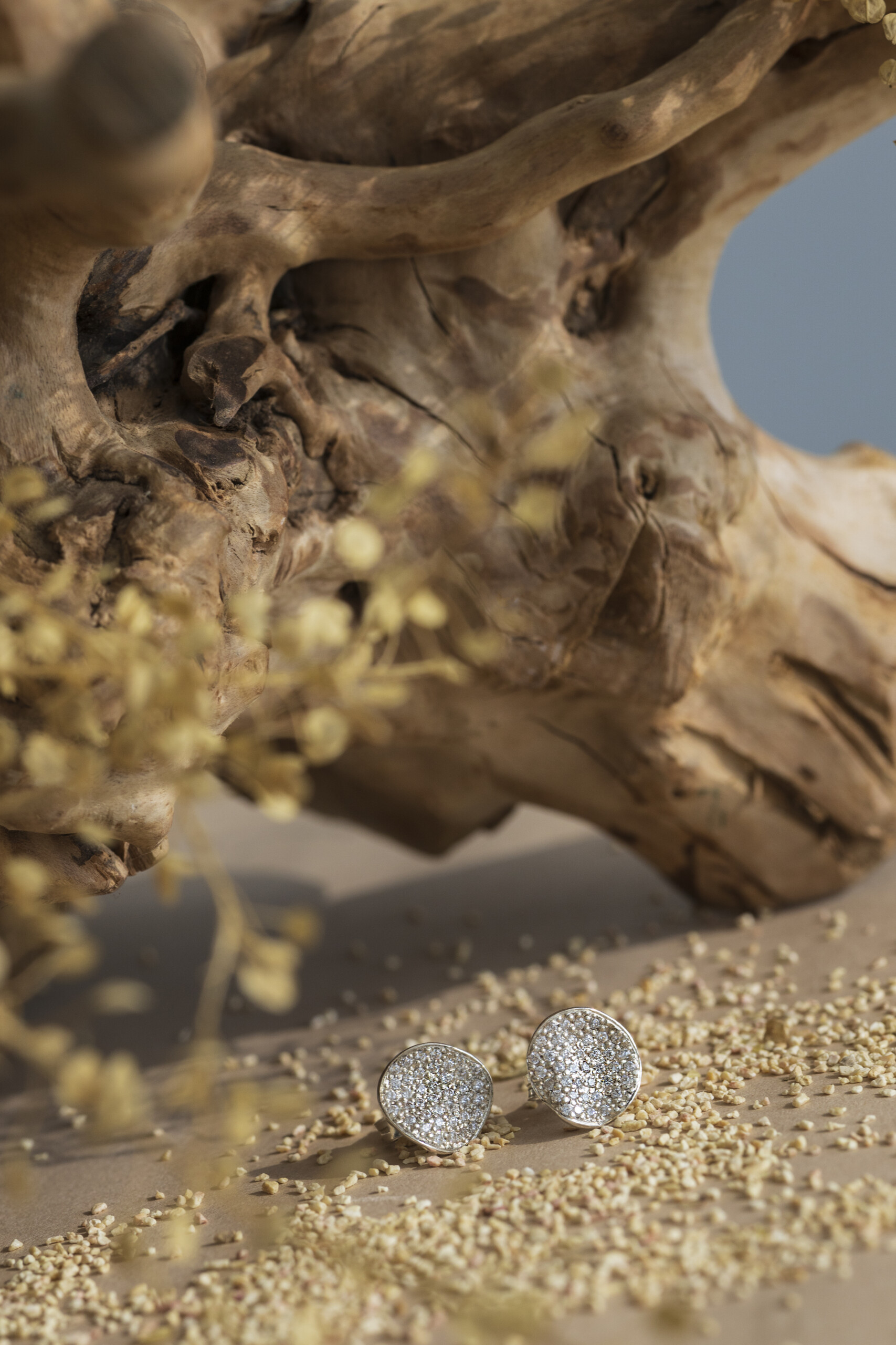 Orecchini Moon con zirconi inseriti in un set naturale di rami e sabbia, evidenziando il legame tra design geometrico e forme naturali.