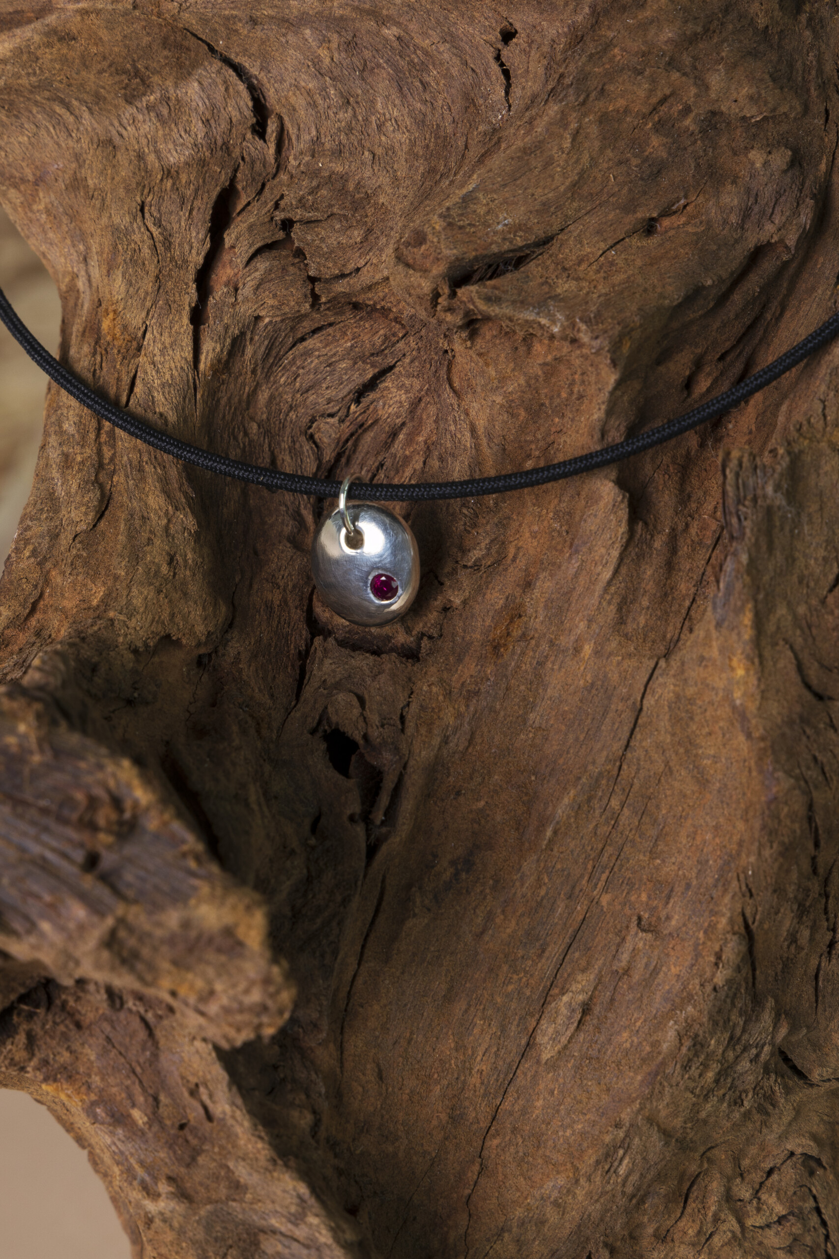 Pendente Pepita con rubino rosso incastonato, poggiato su legno antico; un pezzo unico realizzato a mano nel nostro laboratorio orafo.