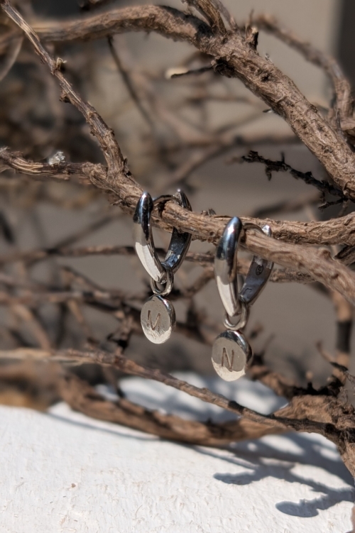 Orecchini a cerchio con ciondoli incisi appesi a un elemento naturale, rappresentanti la filosofia artigianale e su misura di Orme Gioielli.
