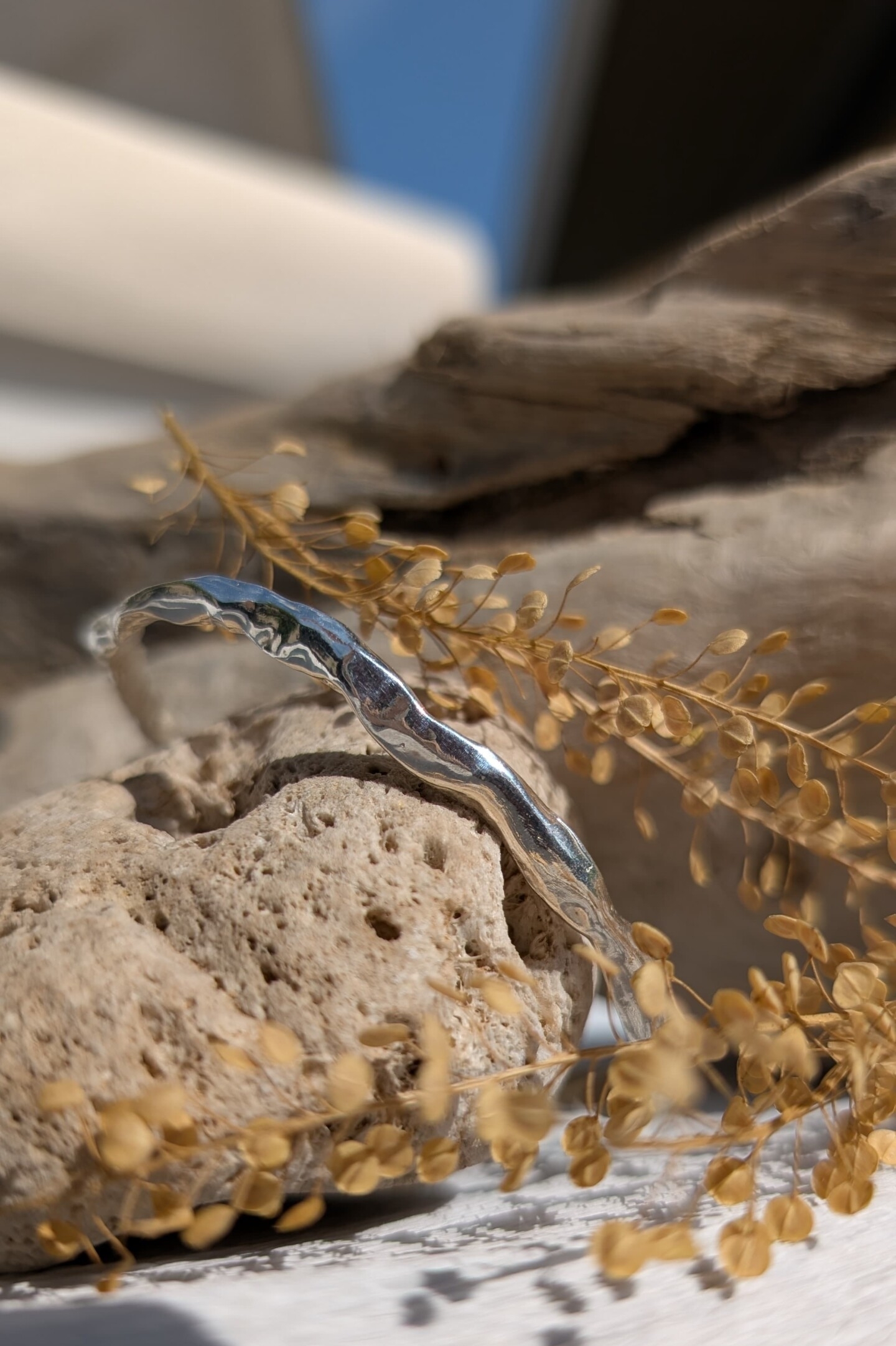 Il bracciale Lava in argento lucido appoggiato su una pietra, mettendo in risalto il contrasto tra la materia grezza e la lucentezza specchiata dell'argento.