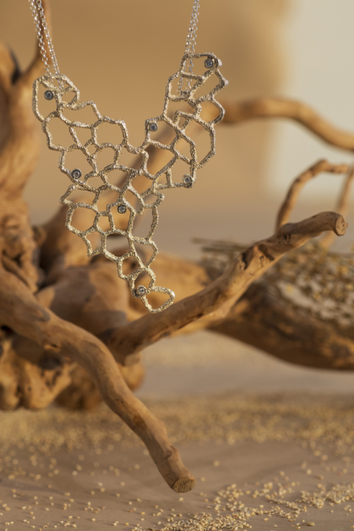 Girocollo scultura della collezione Nebula con grande ciondolo a rete organica in argento 925 lucido e zirconi, sospeso tra rami d'albero dorati.