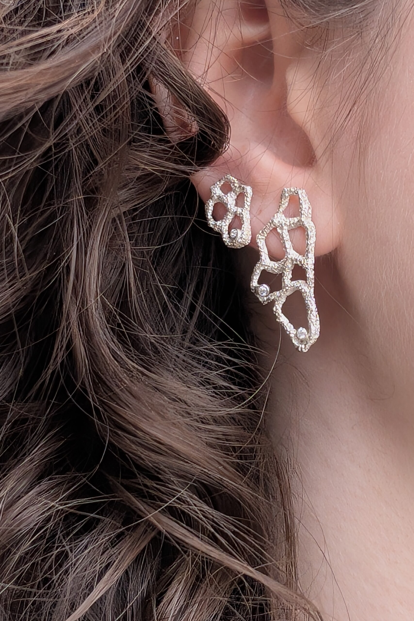 Orecchini a lobo Nebula indossati, mostrati di profilo per evidenziare come la luce colpisca la texture martellata e gli zirconi.