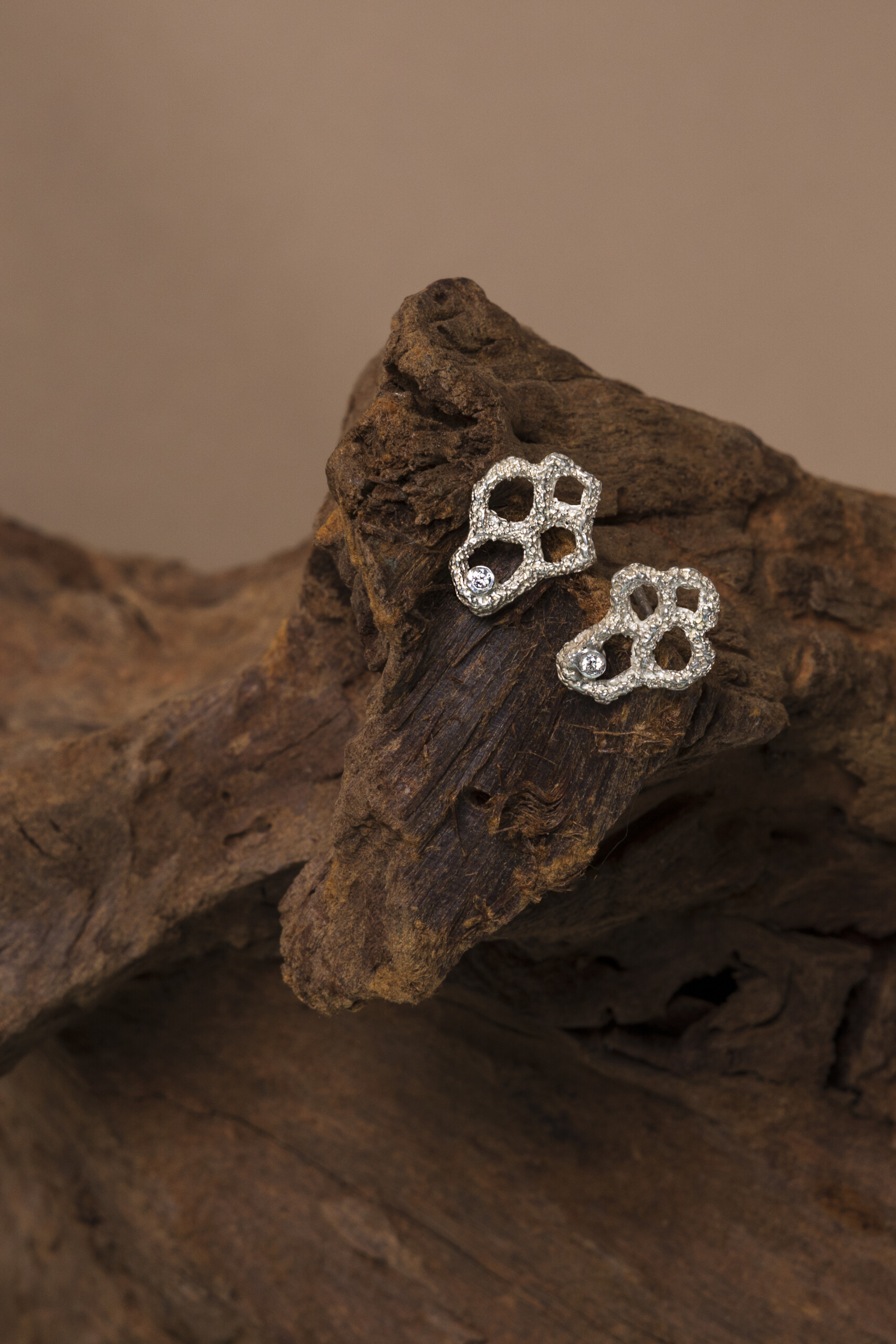 recchini Nebula piccoli in argento appoggiati su legno antico; un esempio di gioielli materici realizzati a mano tramite modellazione in cera persa.