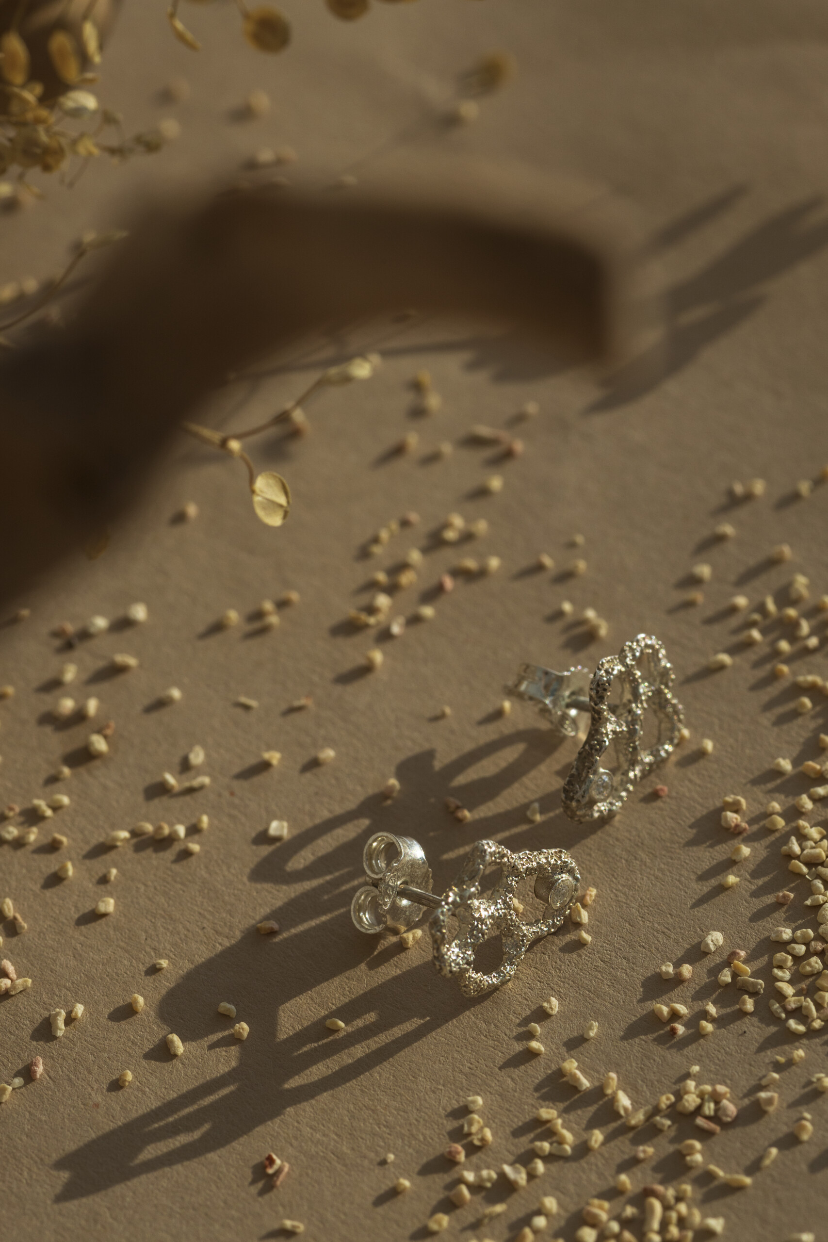 Vista dall'alto degli orecchini Nebula piccoli su fondo naturale; il design geometrico e organico dell'argento si fonde con la lucentezza degli zirconi.