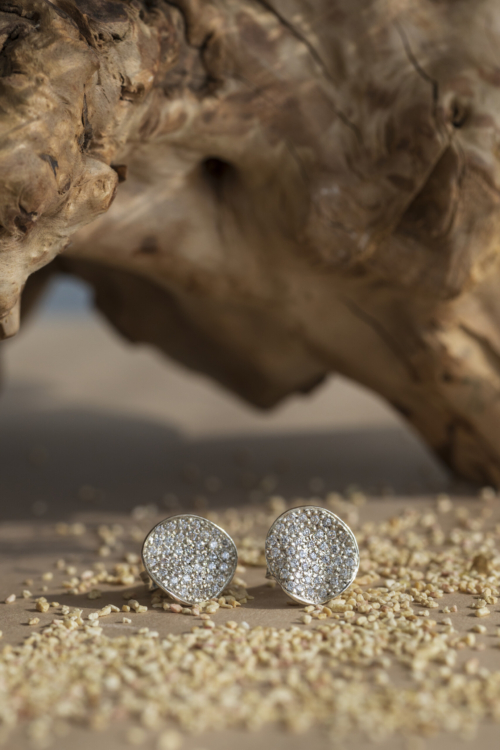 Coppia di orecchini a lobo della collezione Moon in argento 925 con pavé di zirconi, presentati su un fondo sabbioso naturale.