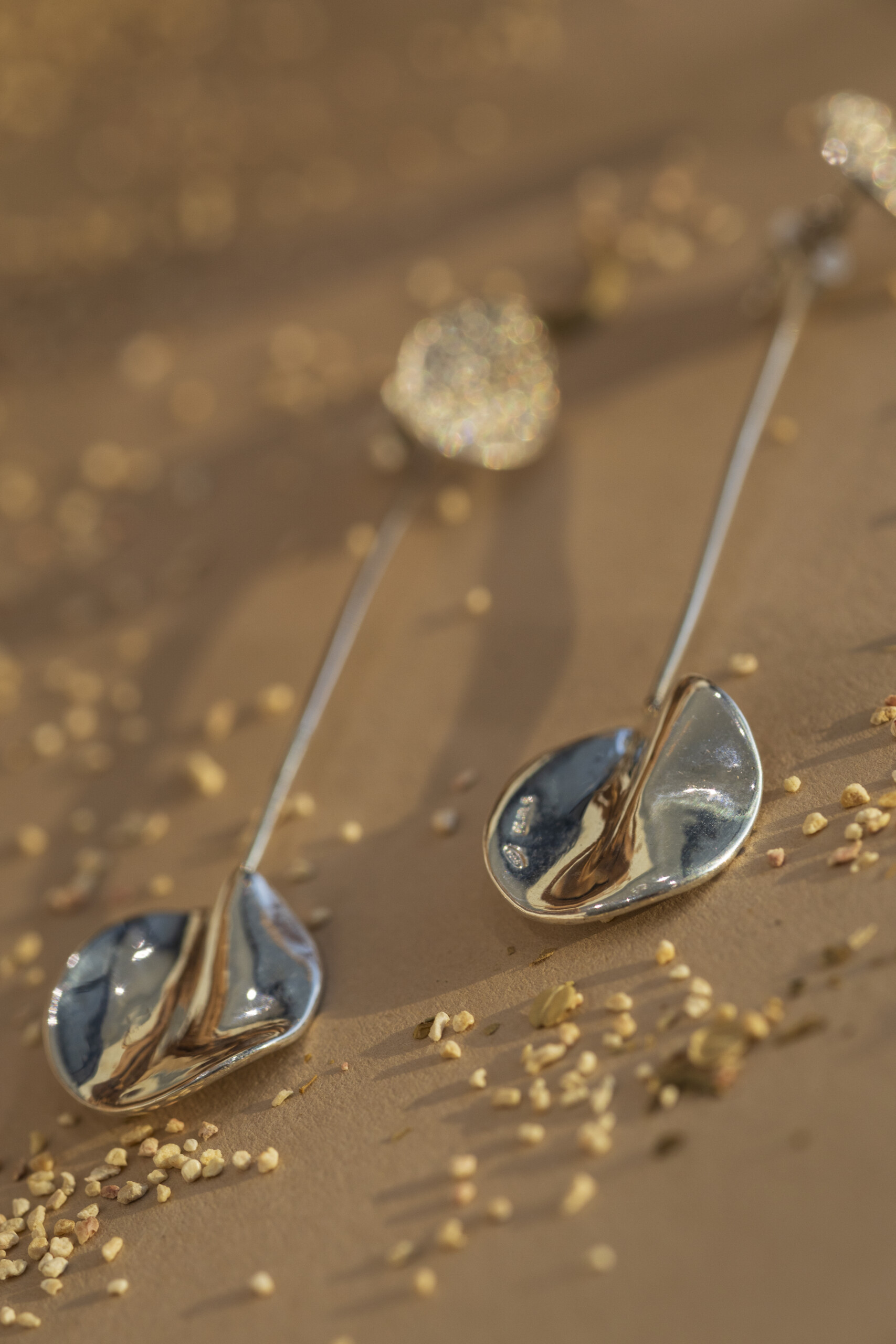 Dettaglio macro degli orecchini Moon pendenti; la superficie in argento lucido riflette la luce naturale, creando un contrasto materico con il pavé di zirconi.