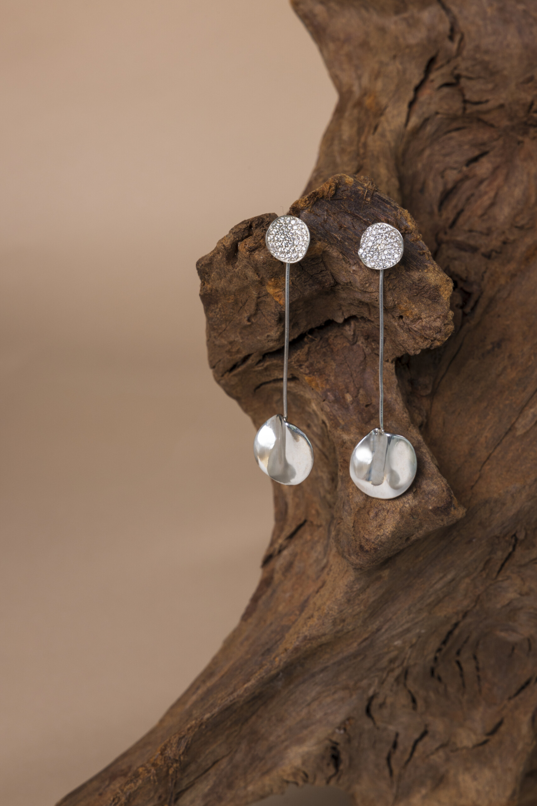 Orecchini Moon pendenti presentati su una radice di legno antico; la lavorazione artigianale dell'argento e l'incastonatura degli zirconi rendono ogni paio un pezzo unico.