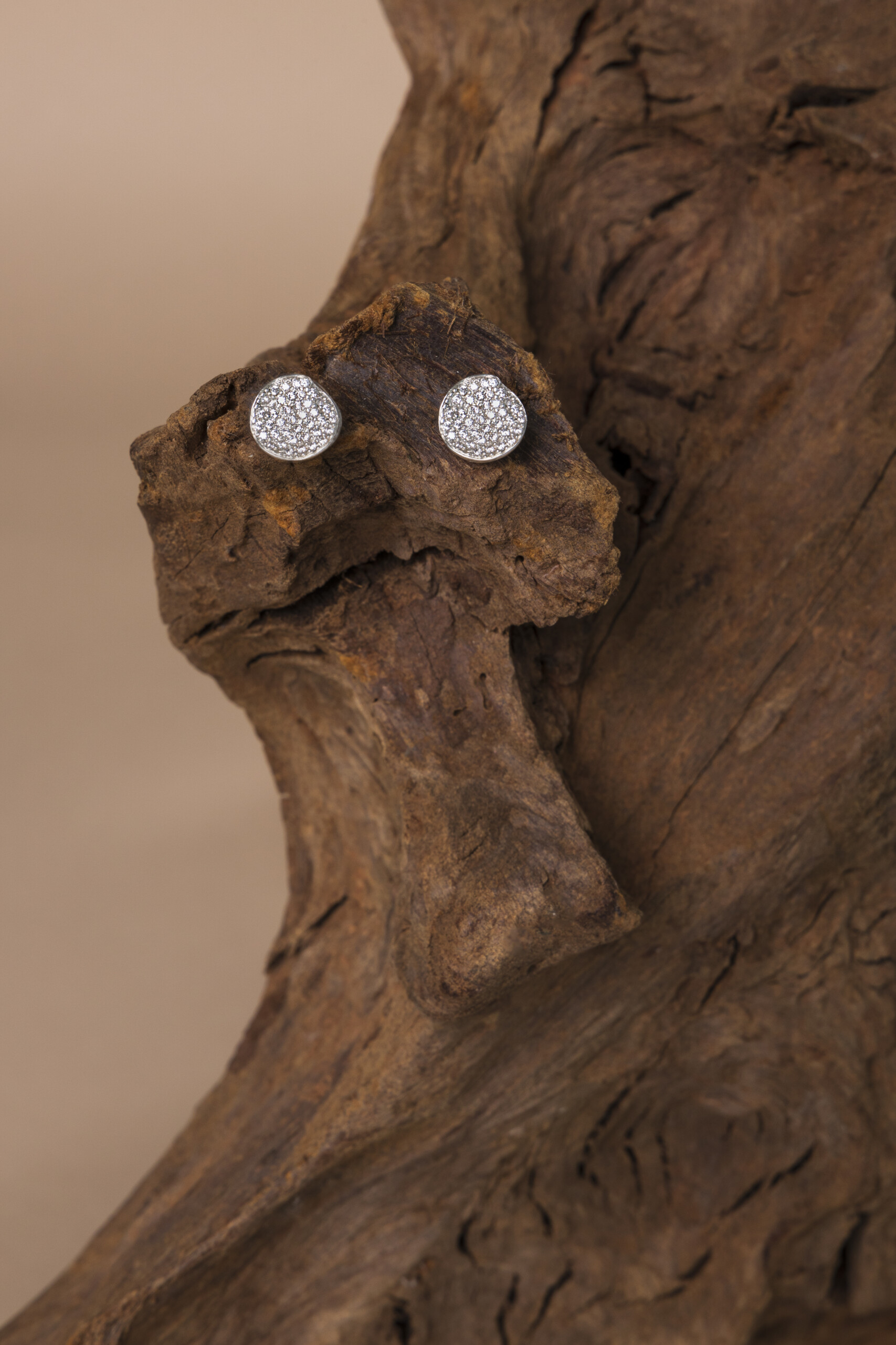 Orecchini artigianali Moon con zirconi incastonati, poggiati su legno antico; un gioiello materico modellato interamente a mano nel nostro laboratorio.