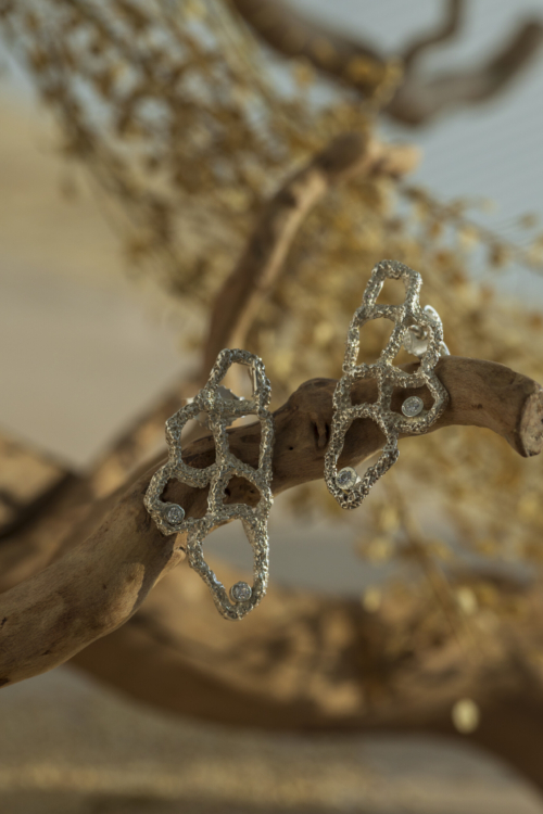 Coppia di orecchini scultorei della collezione Nebula in argento 925 e zirconi, adagiati su un ramo naturale; un perfetto esempio di gioielli materici e unici.