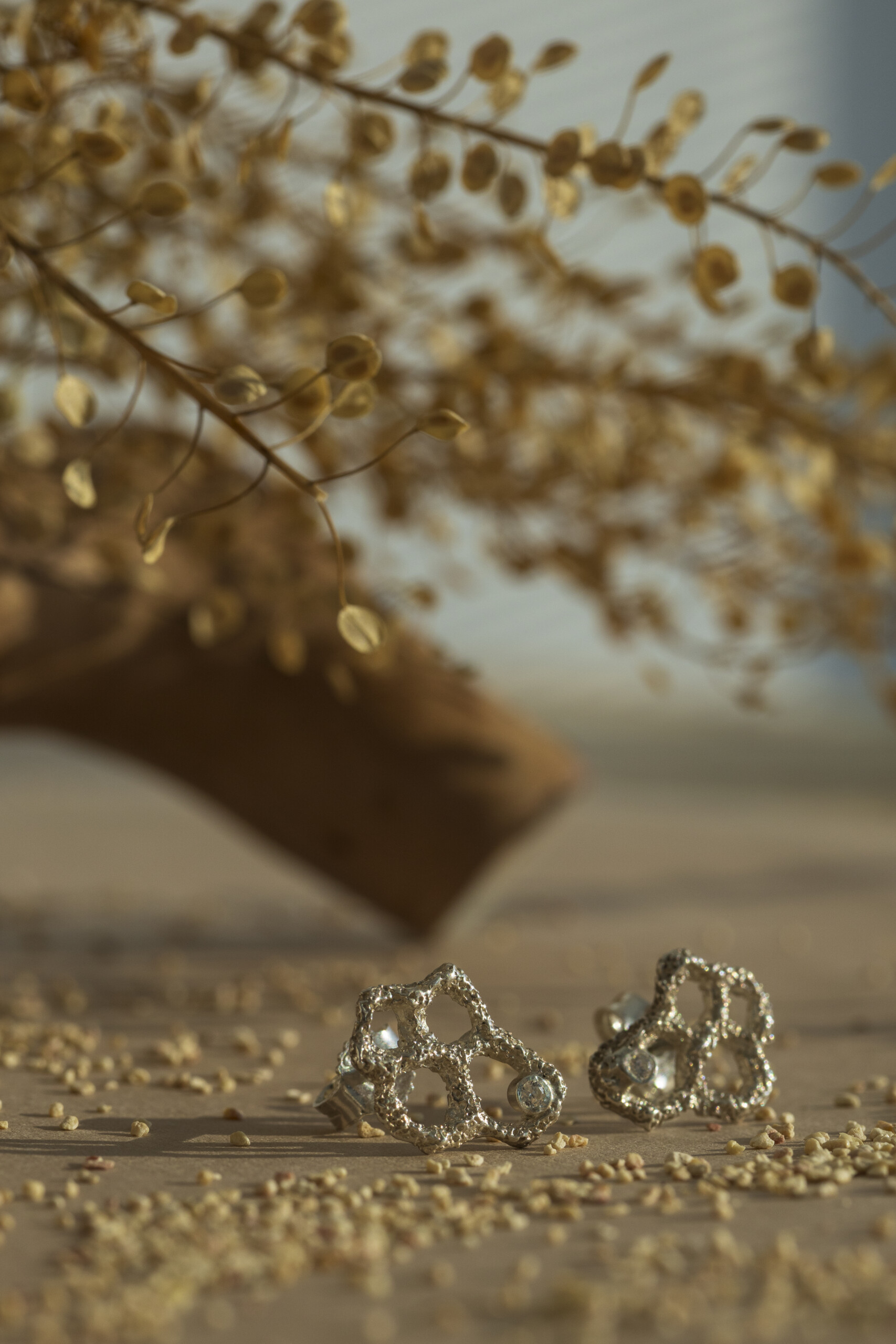 Coppia di orecchini piccoli a lobo della collezione Nebula in argento 925 con zirconi, caratterizzati da una texture materica organica e poggiati su un fondo sabbioso.