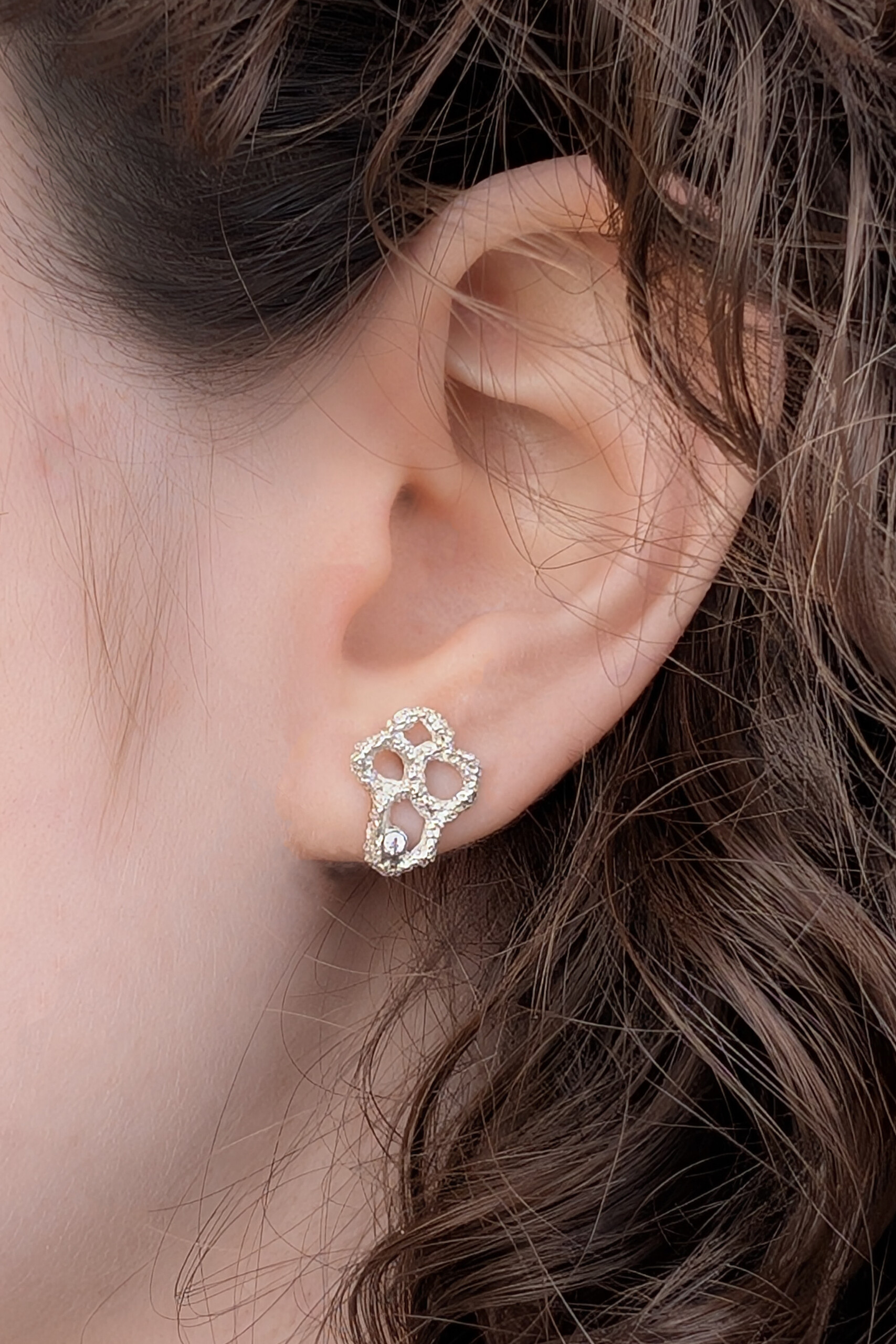 Foto macro di un orecchino piccolo Nebula indossato; la lavorazione artigianale a rete in argento risalta per la sua eleganza minimalista e materica.