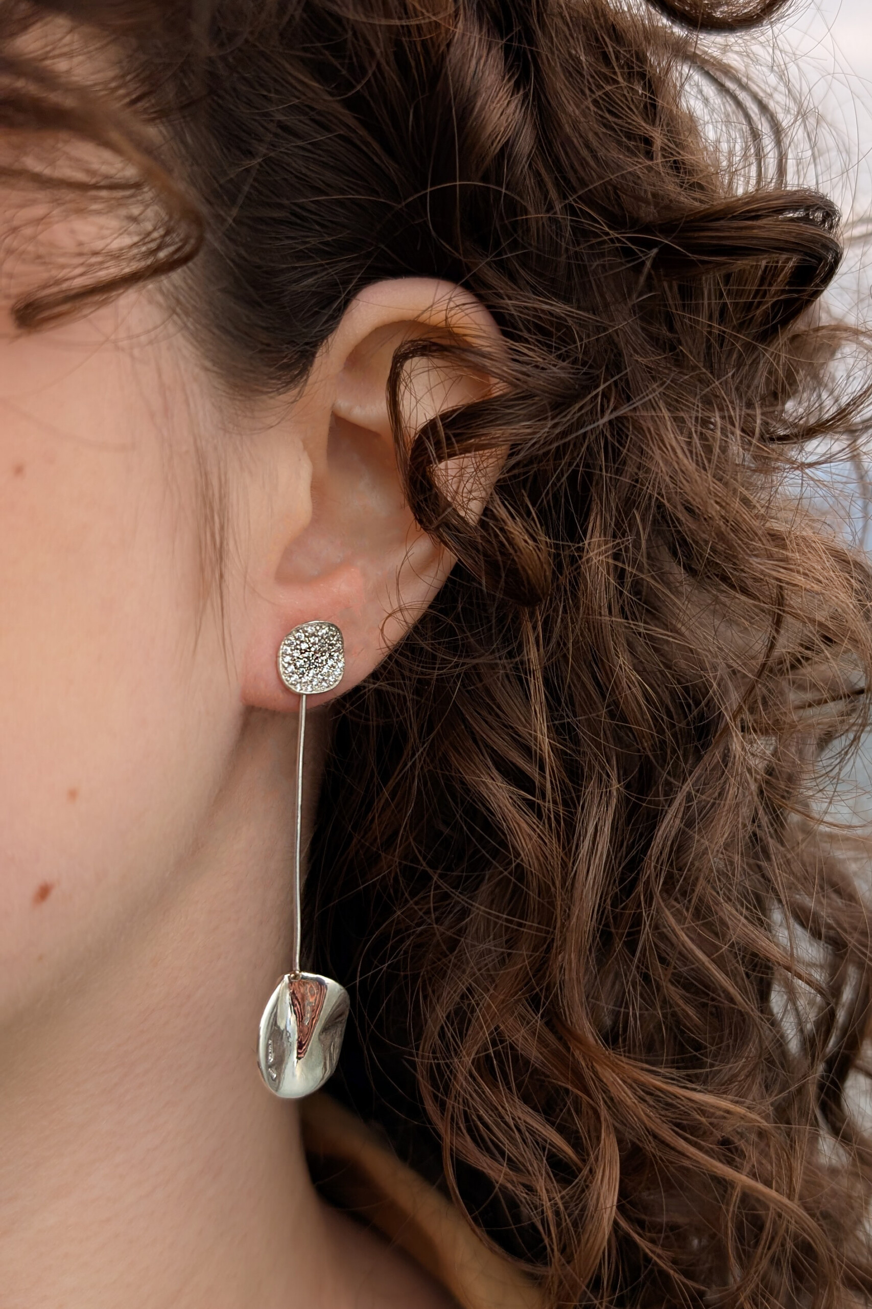 Foto lifestyle dell'orecchino Moon nella versione pendente grazie all'asticella in argento; un gioiello scultoreo e versatile per un look sofisticato.