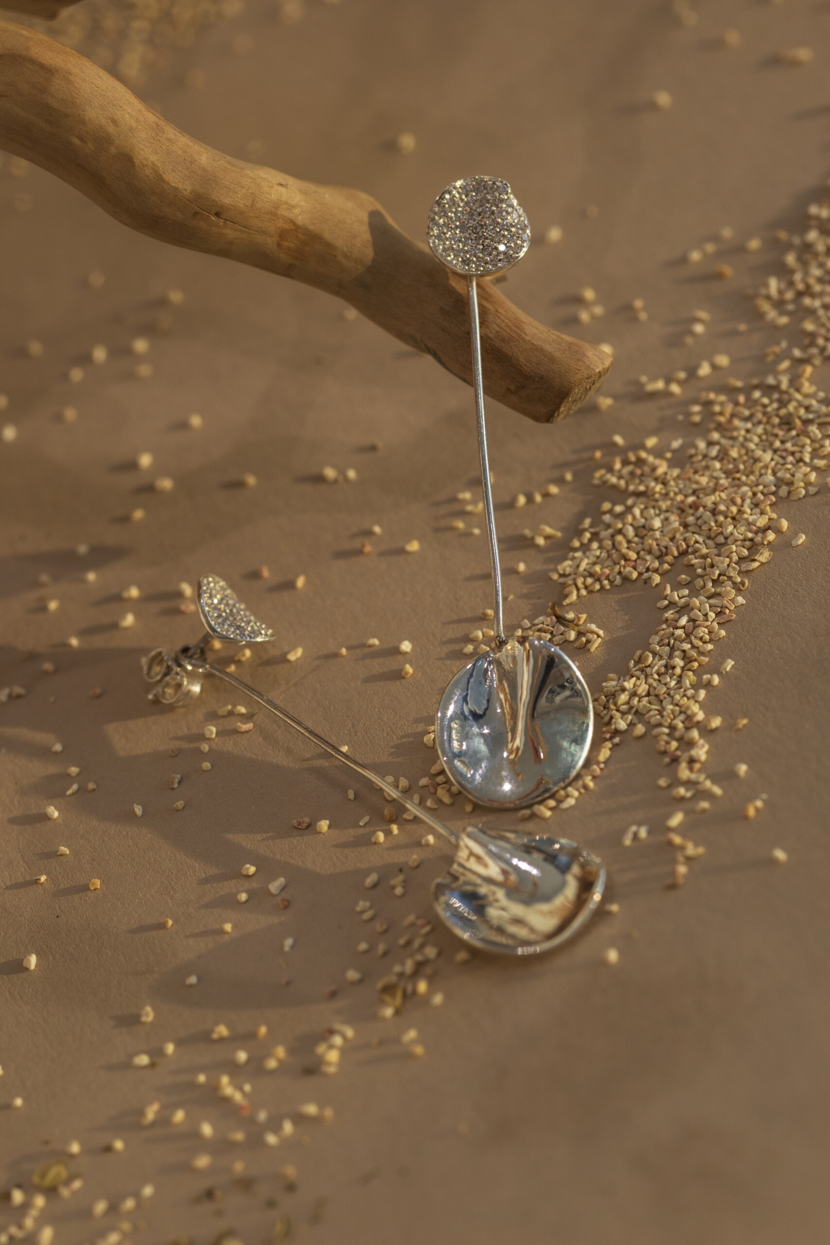 : Coppia di orecchini pendenti della collezione Moon in argento 925, caratterizzati da un elemento a lobo in zirconi e una lastra ondulata pendente, appoggiati su rami.