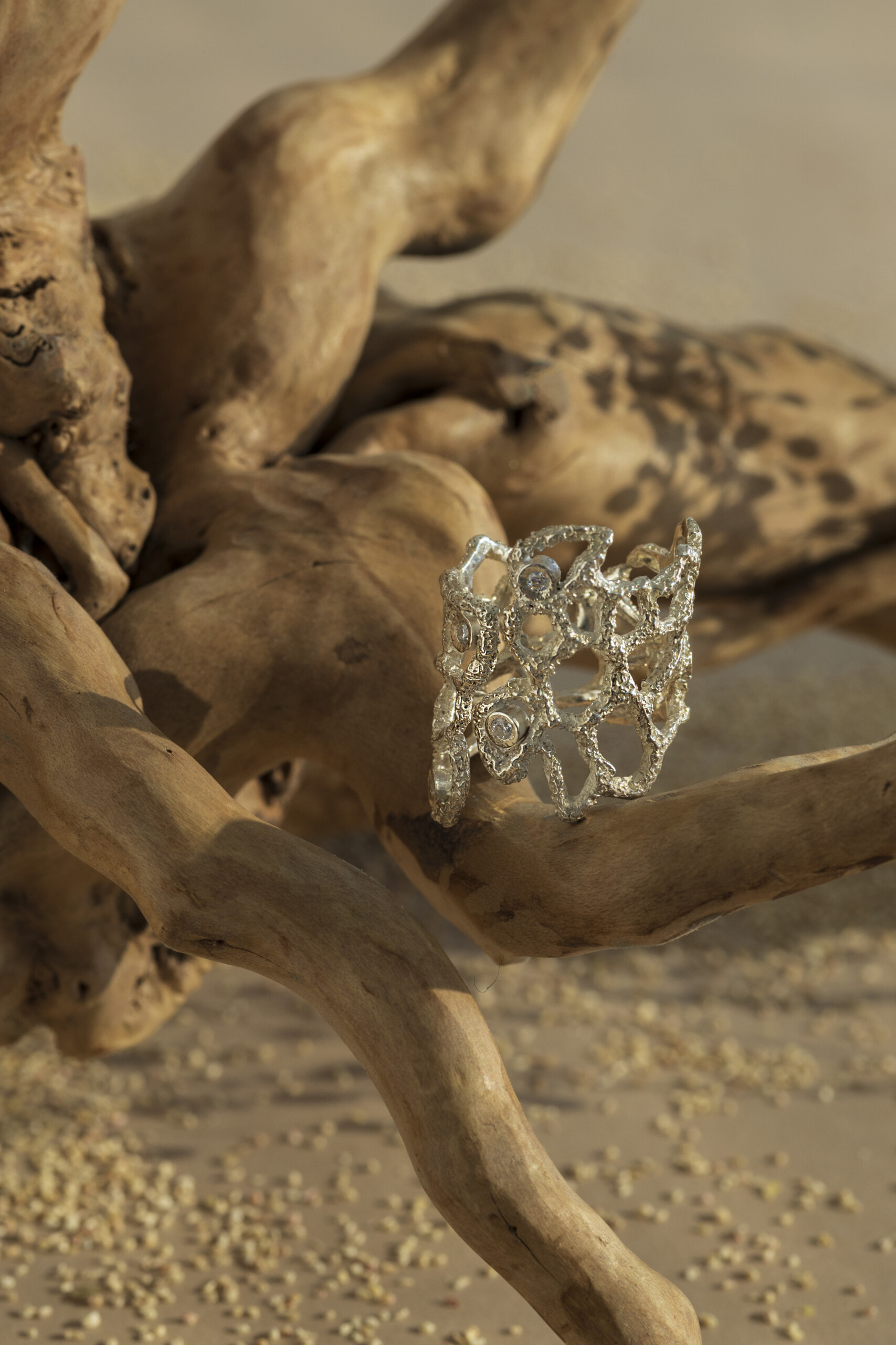 Anello Nebula con zirconi incastonati tra gli intrecci d'argento, adagiato su una radice chiara che ne esalta la texture materica e il design naturale.