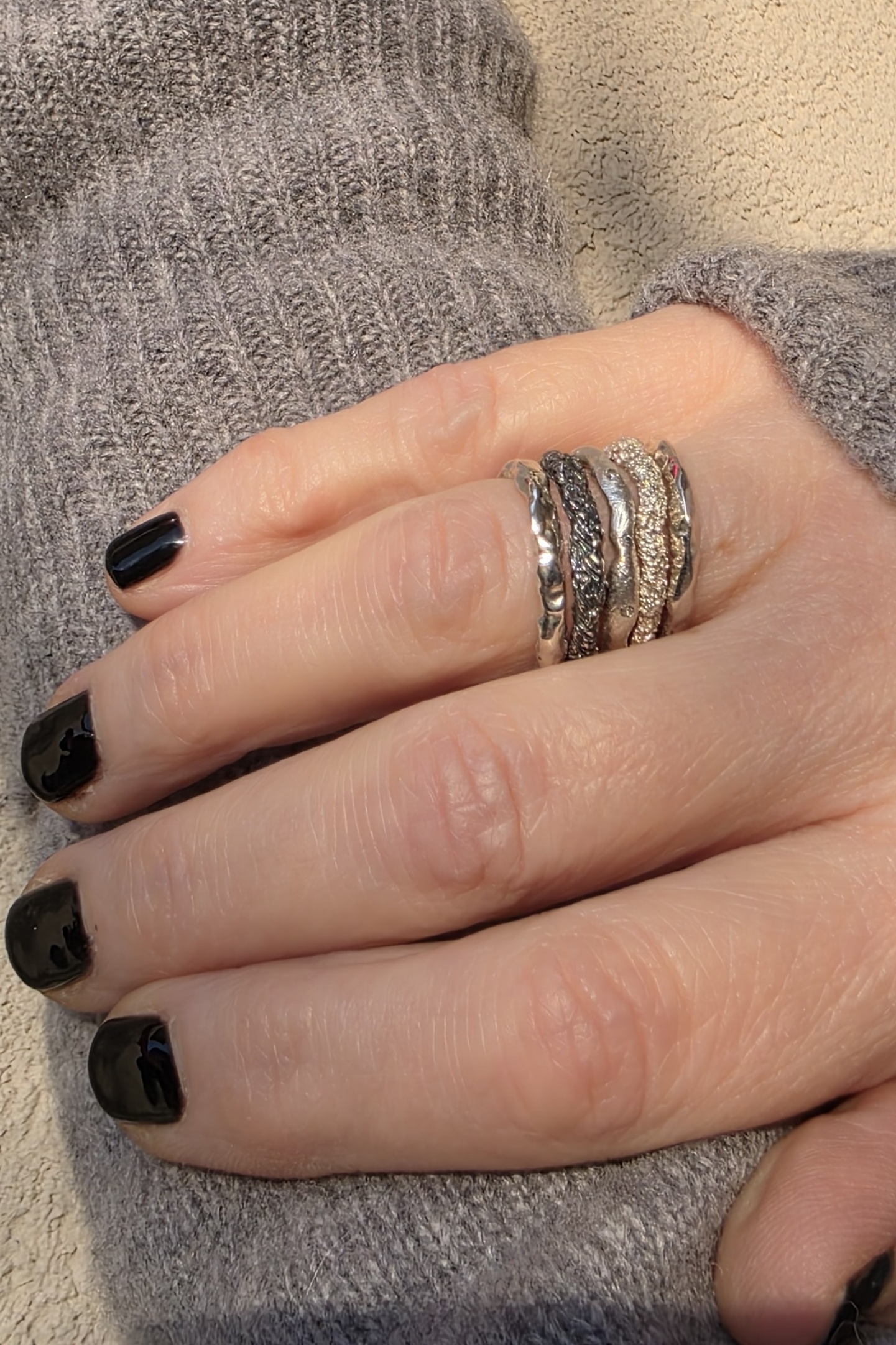 Mano con set di anelli componibili in argento 925 naturale e brunito materico.