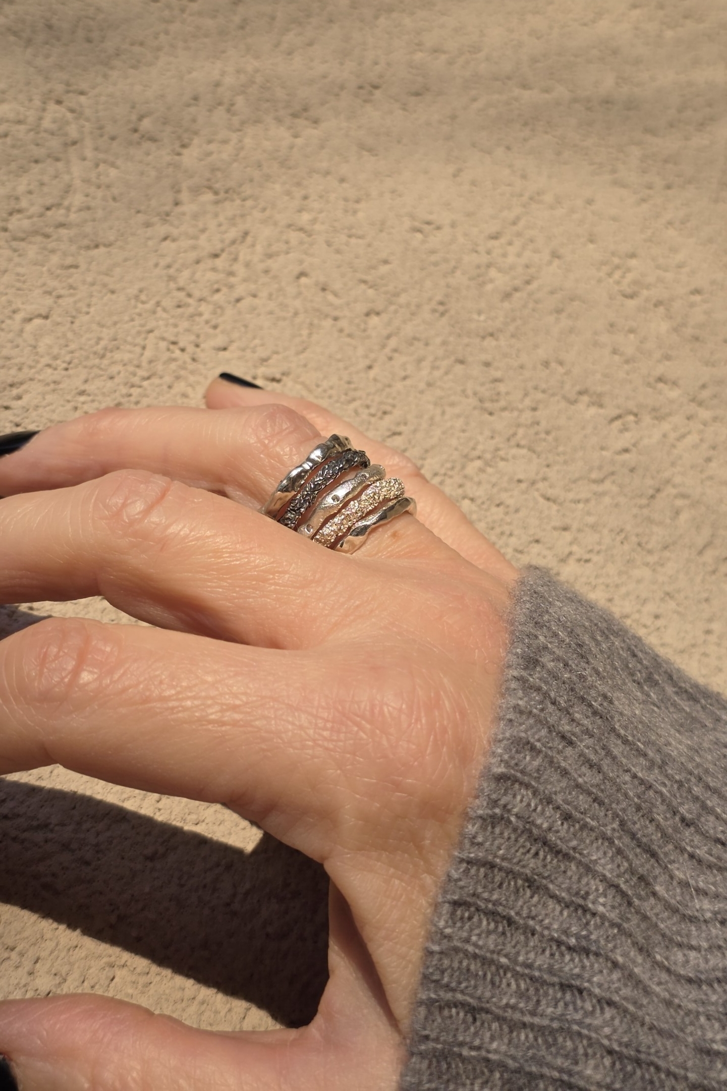 Mano che indossa il set completo Caleidos: cinque anelli componibili in argento artigianale e diamanti naturali sovrapposti.